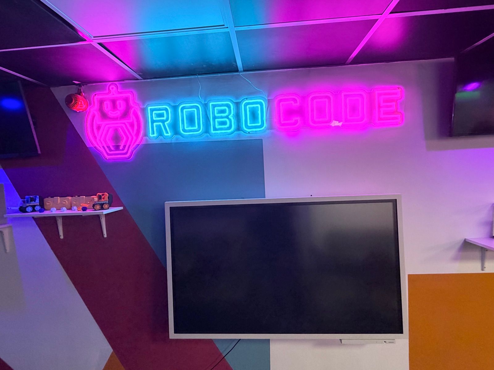 The neon Robocode sign over a display screen