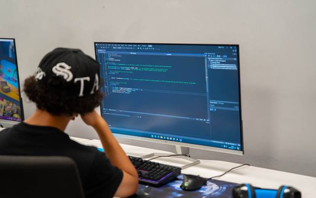 A Robocoder writing code at a large monitor