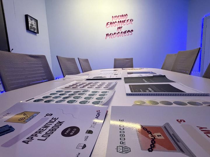 The Apprentice and Academy logbooks in front, with the Playbook and sticker sheets along the table